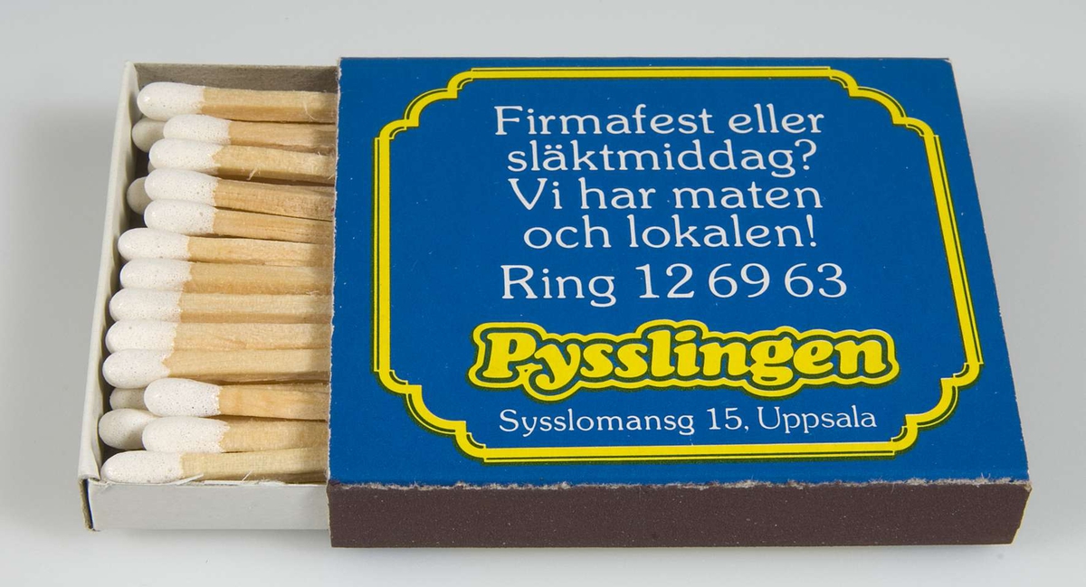 Blå och gul tändsticksask av papp med reklamtext för restaurang Pysslingen, Sysslomansgatan 15, Uppsala. Vitt svavel på tändstickorna.