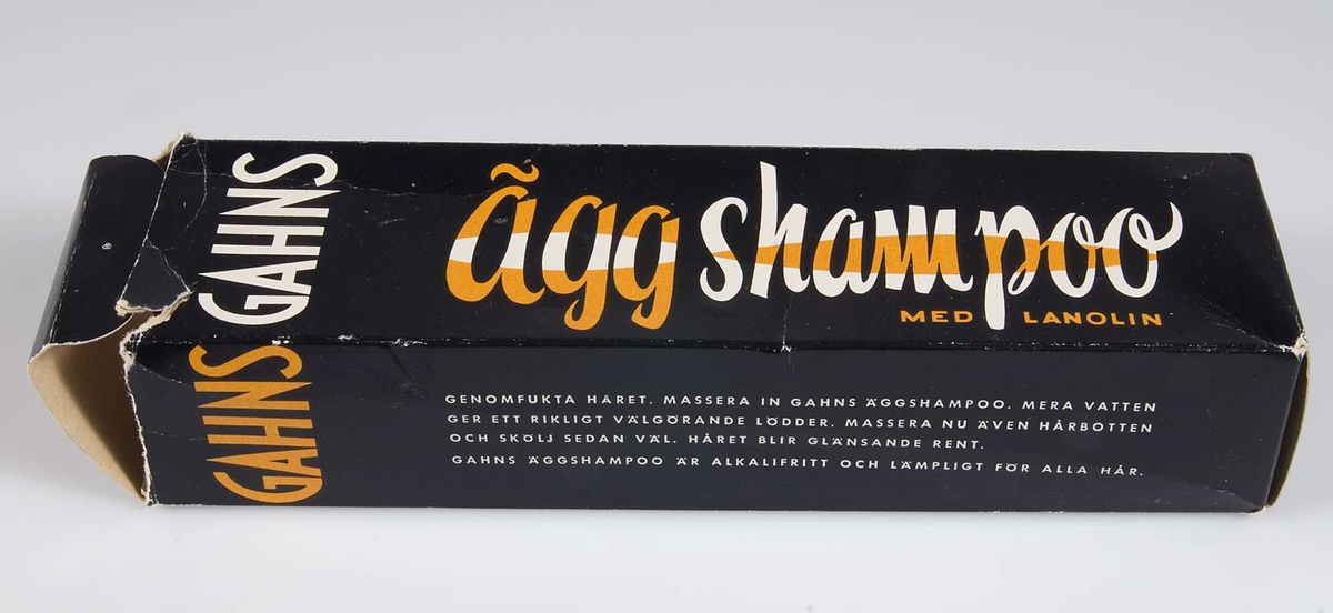 Förpackning av svart papp med text i vitt och orange: GAHNS äggschampoo med lanolin, samt bruksanvisning. Tub av plåt med samma text i gult i stället för orange. Skruvlock av gul konstmassa.
