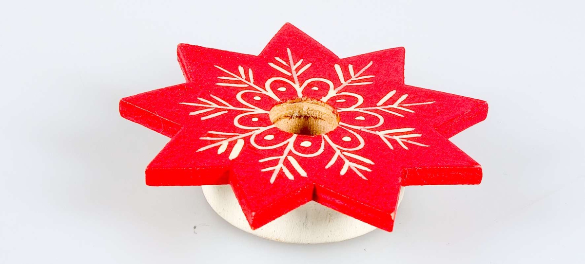Julljusstake av trä i form av en stjärna. Ljusstaken är målad i rött och vitt.
På undersidan av ljusstaken står med bläck "Y.1144 0:85[?]".