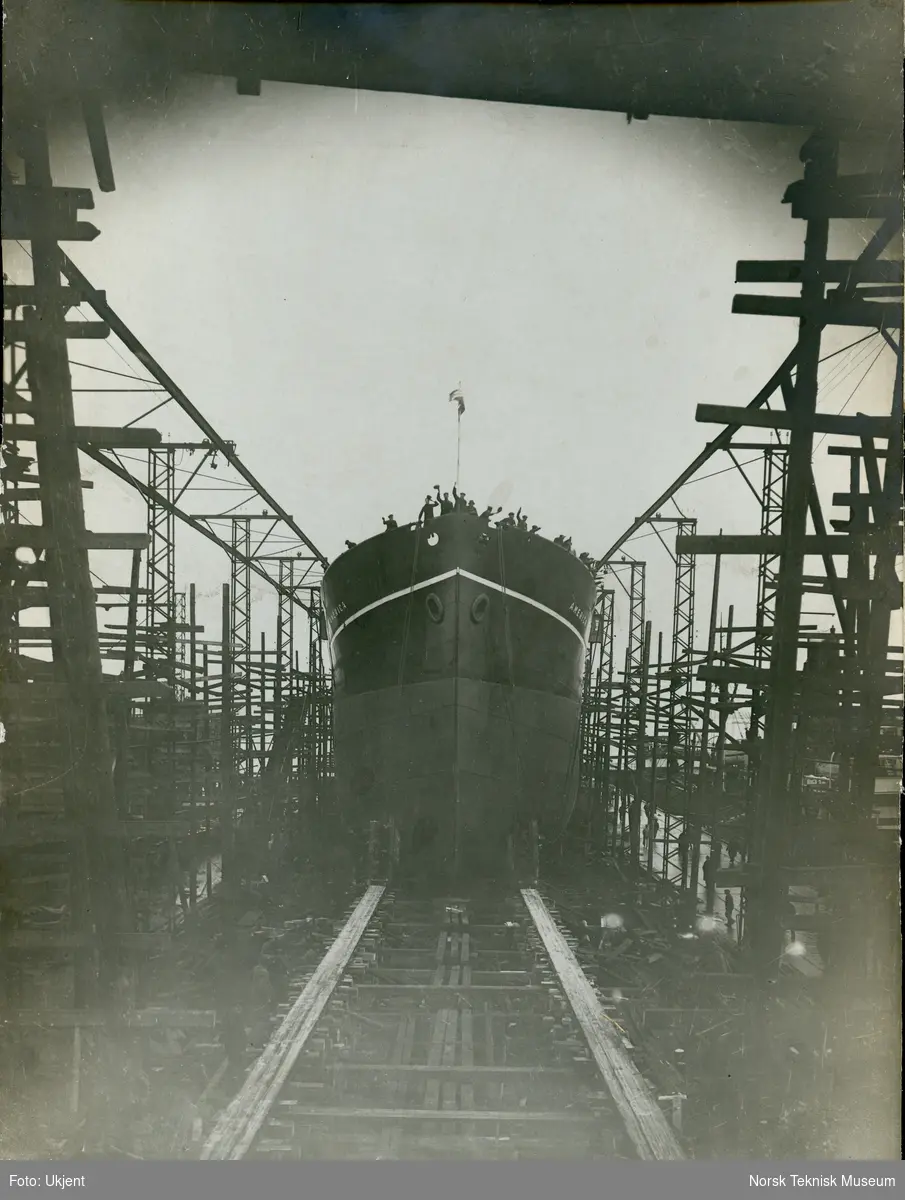 Stabelavløpning, lastebåten M/S America, B/N 389 på Akers Mek. Verksted. Skipet ble levert av Akers Mek. Verksted i 1921 til W. Wilhelmsen, Tønsberg. Omtrent 18 menn vinker fra dekk.