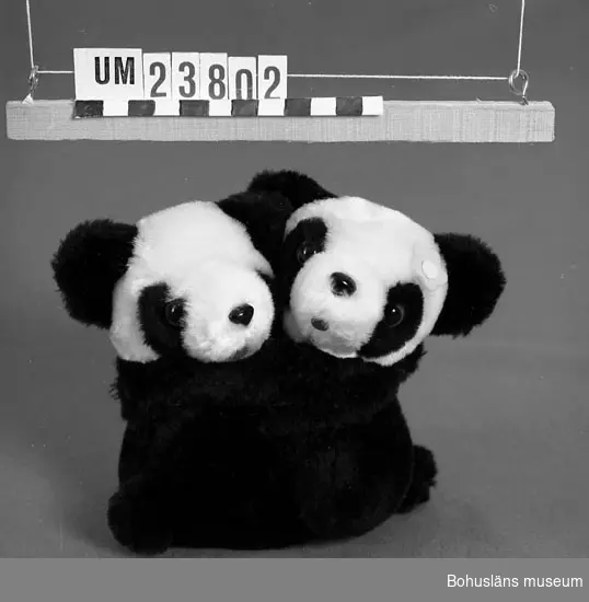 Två pandor som kramar varandra, hopsatt med kardborrknäppning, svarta med
vita huvuden. På den ena en blomma av papper i rosa. Ögon av glas