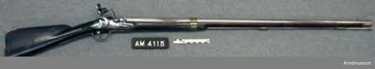 Karbin med flintlås.
Kulvikt 18,3 gr. "Av denna modell finns en variant, AM 4115, som blott i fråga om kalibern, 16 mm, piplängden, 92,6 cm, och vilken 3,85 kg samt i att laddstocken är av stål skiljer sig från den ovan beskrivna.