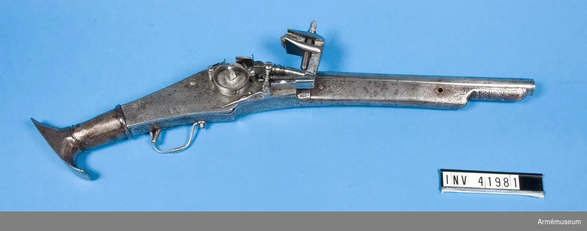 Grupp E II.
Hjullåspistol, 1500-talets slut, Tyskland.

Pistolen är helt av järn. Pipan är rund med avfasde sidor på kammarstycket. Den har spår av en graverad dekor på bakre delen.

Låsblecket har etsad deko, har en skyddskåpa som ej täcker hjulets ytterkant. På låsblecket finns två stämplar: En med en hare samt bokstäver K S, samt en något otydlig stämpel som är Nürnbergs kontroll-stämpel (troligen Stöckel nr. 1593).

Stocken är av järnplåt med etsad dekor. Kolven har en T-formad avslutning.

2009-12-08 EW
Fängppannan saknas.