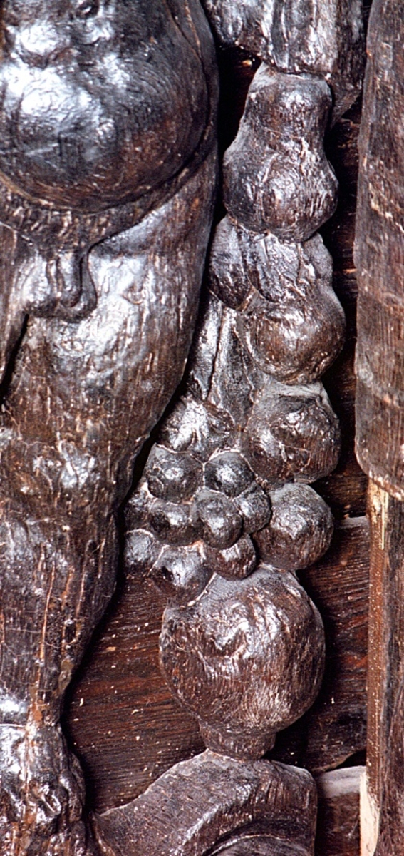 Skulptur av en putto stående på postament med omgivande ornamentik.
Putton har ett frodigt och undersätsigt utseende, med avrundade former. Puttons vänstra hand vilar på en sköld, medan höger hand är uppåtsträckt, hållande en olivkvist.
Ovanför putton sitter ett veckrikt draperi, "upphängt" på en stång med profilerad ände. Där det nedhängande draperiet slutar vidtar tunga fruktfestoner som når ned till postamentet, vilket är dekorerat med symmetriskt ställda rullverksspiraler. Rullverksspiralerna är utformade så att de bildar krumma vädurs- eller gumsehorn till ett i postamentet utsnidat djurhuvud.
Puttons ansikte, vänster arm samt mage är snidade separat. Skulpturens baksida är slät.

Text in English: Sculpture of a putto, standing on a base surrounded by ornamentation.
The exuberant plump cherub has a well-rounded body. Right hand rests on a shield. The left hand holds an olive branch aloft.

Above the putto''s head hangs a heavily-folded drapery. The drapery forms a swag as it hangs from a curtain rod. The prominent ends of the curtain rod are carved in relief. Heavy festoons of fruit flow from the drapery ends to the feet of the putto. The symmetrical scrollwork on the base takes on the appearance of ram''s horns when combined with the imprecise representations of animal heads.
Face, left arm and belly are carved separately. Reverse side is smooth.