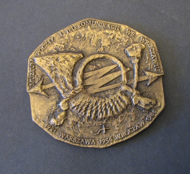 Medalj, sexkantig, i brons från Polska post- och telekommunikationsmuseet i Wroclaw.

Åtsidan visar ett posthorn som har handgreppet lindat med ett tvinnat, tunt rep. Bakom posthornet, horisontellt, syns en blixt med pilar i var ände. Runt medaljens kant löper en text som lyder "MUZEUM POCZTY I
TELEKOMUNIKACJI WEWROCKLAWIU" samt "1921 WARZAWA 1956 WROCKLAW 1986".

Frånsidan visar ett motiv med 7 st posthorn. Överst finns tre st. Mitt
på ligger två liknande lurar. Till höger ett litet. Ett större
nederst på medaljen. I det större hornets slinga finns ett "W"
omgärdat avtexten "ZA ZASLUGI DLA MUZEUM".
