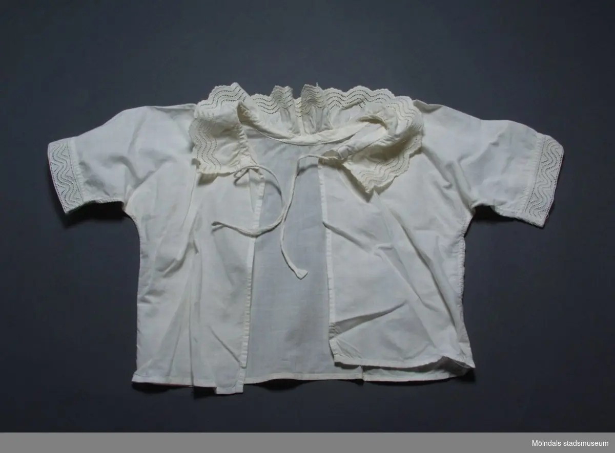 Spädbarnssskjorta i bomull med brodyr runt halsringning och ärmar. Gulnad.