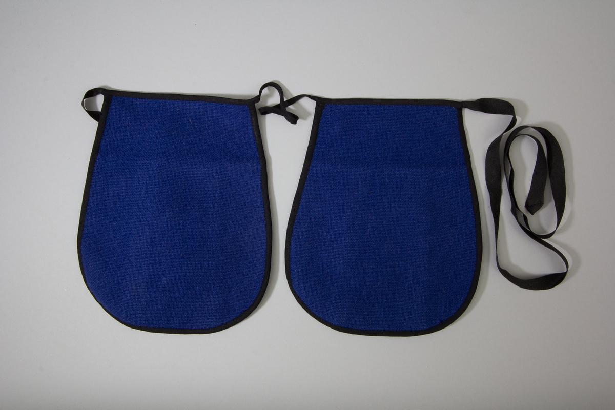 Kjolsäck till dräkt för kvinna från Östervallskog socken, Värmland. Modell med avskuret framstycke. Tillverkad av grovt, kanske handvävt tyg, tuskaft, i två färger. Framstycket gjort av tre delar, rött i mitten och och blått på sidorna. Ofodrat. Bakstycke och överstycke av blått tyg. Kantat runtom med svart diagonalvävt ylleband. Två stycken kjolsäckar fästa, en på var sida, på ett knytband diagonalvävt av ullgarn.