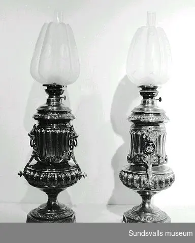 Två fotogenlampor med fot i mässing och kupa i glas.
