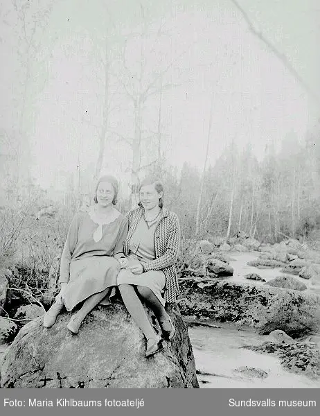 Porträtt, två flickor sitter på en sten vid en bäck.
