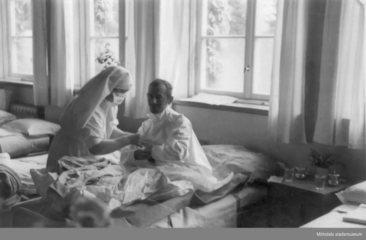 "Karantänsförläggning" på Kvarnbyskolan för överlevande från koncentrationsläger i Tyskland och Polen 1945.  
Skolan fungerade under denna sommar som beredsskapssjukhus.
 
Manlig patient i sjuksäng och en sköterska.