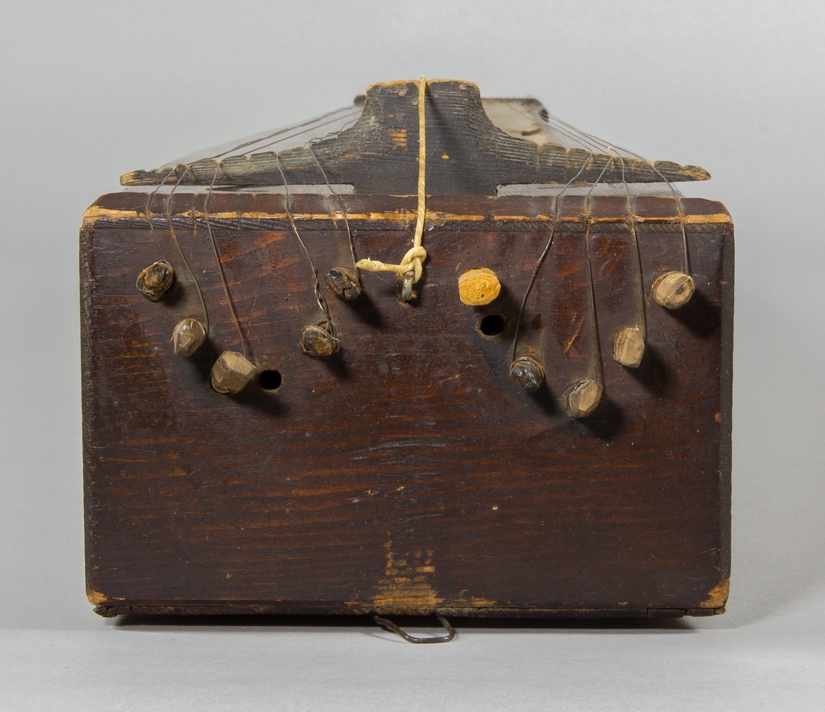 Psalmodikon från Nöbbele, Småland, från c:a 1850. Låda av trä med en sträng, plats för 12 bordunsträngar. Lätt utsvängda sidor, S-formade ljudhål. En remsa av papp med siffror för notlägen monterad på ena sidan om tonbrädan.