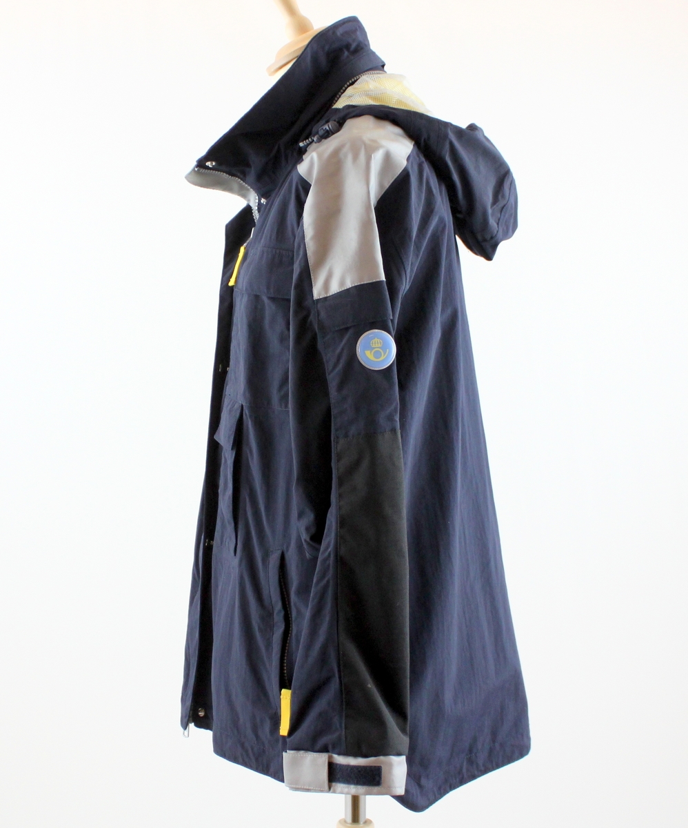 Jacka, mörkblå med en postsymbol modell 2001 i ett ljusreflekternade material på vänster ärm. Jackan har tre klaffförsedda fickor samt två sidfickor som försluts med dragkedja. Ok och ärmlinning försedda med fastsydda reflexband.