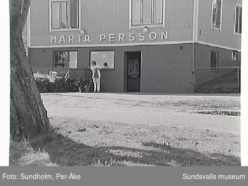 Fotodokumentation av Märta Persson, livsmedelsaffär i kv Mandeln 1, Majorsgatan 17, Sundsvall.1 juli 1922 övertog Märta Persson (gift Claésson) mjölk- och speceriaffären. Affärsnamnet blev hennes flicknamn. Fram till 1980-talets mitt arbetade hon dagligen i butiken. Den förestås nu av dottern, Kerstin Sunding.