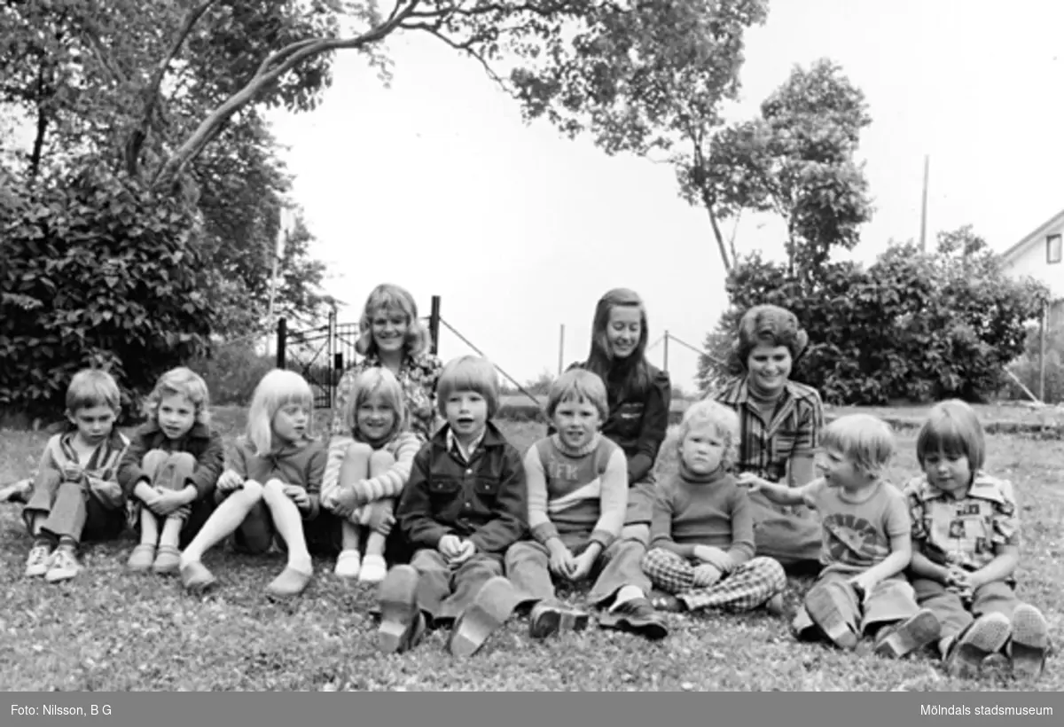 Några barn och tre fröknar sitter i gräset. Holtermanska daghemmet 1973.