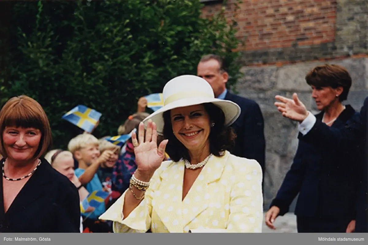 Museichef Mari-Louise Olsson och Drottning Silvia utanför Mölndals Museum 1997. Bakom drottningens hatt ses en av säkerhetsvakterna. Besök av kungaparet på Mölndals Museum 1997-08-27 i samband med att Tjenstefolksbyggningen på Gunnebo slott invigdes.