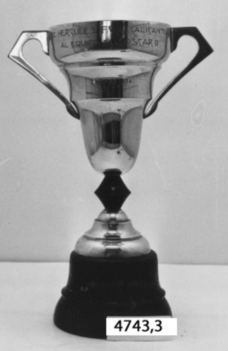 Pokal av nysilver, stående på fot av trä, svartmålad. Utgör pris i rodd.
Ingravering: El Herculles F.C. De Alicante Al Equipo Del Oscar II 20 - XII - 1934.