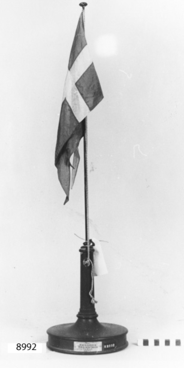 Bordsstång/bordsflagga försilvrad med fot av mahogny. Med svensk örlogsflagg av siden.