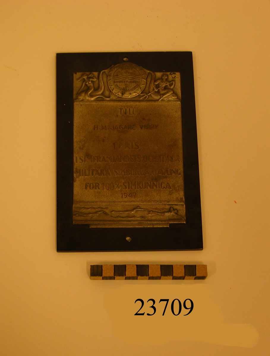 Plakett av silver fäst på platta av bakelit. Text: TILL H M JAGARE VISBY 1 PRIS I SIMFRÄMJANDETS OCH DN:S MILITÄRA SIMBORGARTÄVLING FÖR 100% SIMKUNNIGA 1947.