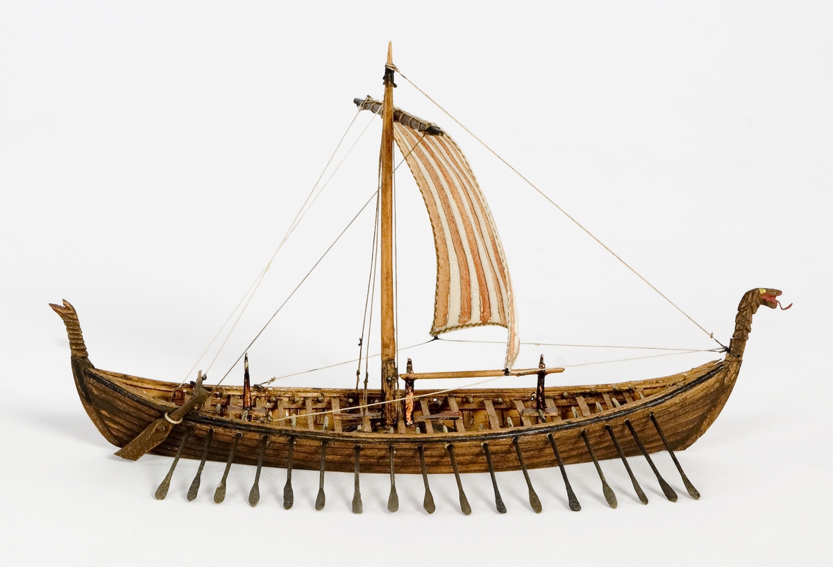 Fartygsmodell, vattenlinjemodell, hel i block av trä, vikingaskepp ("Osebergsskeppet") 800-t. Klinkbyggd, brunt skrov med höga stävar. Riggad med 1 mast, vit- och rödrandigt råsegel. I förstäven drakhuvud. Utrustad med 17 par åror samt styråra (sidoroder).Föremålets form: Vattenlinjemodell