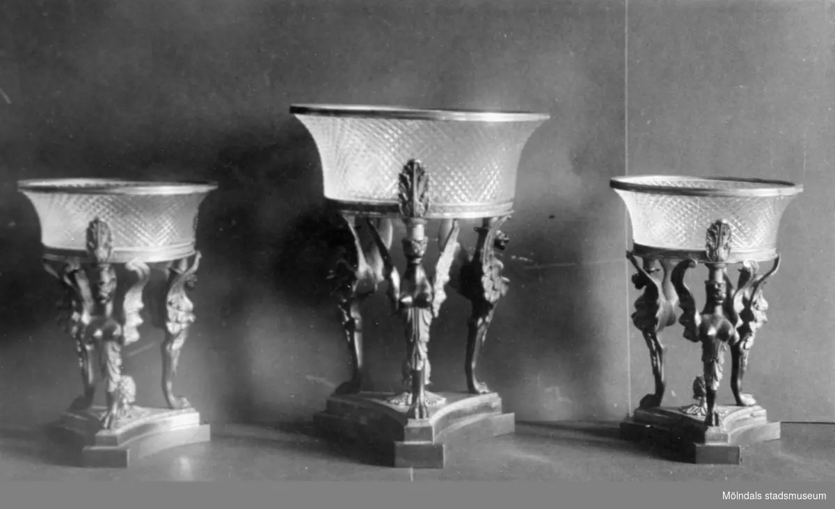 Tre glasskålar i samma utformning varav en är något högre. Varje skål bärs upp av tre figurer ståendes på en platta. Gunnebo slott 1930-tal.