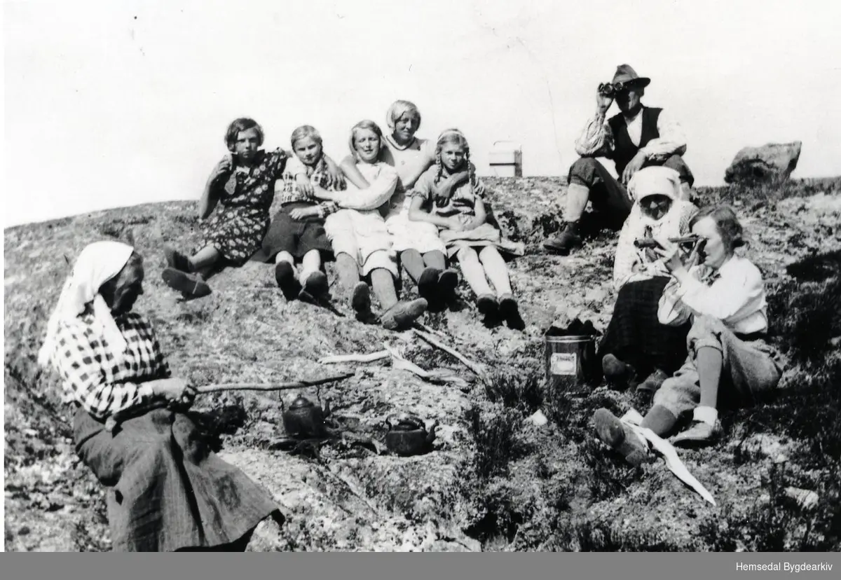 Biletet er teke i Holdeskaret i 1936.
Frå venstre: Ingeborg Møllerplass med kaffikjel; Karoline ev. Birgit Dokk, Magnhild Flaget; Anne Bråten; Maria Holde; Birgit Flaget; Anne Bråten (Snikkerbrøta).
Mannen bak og dama til høgre er byfolk.