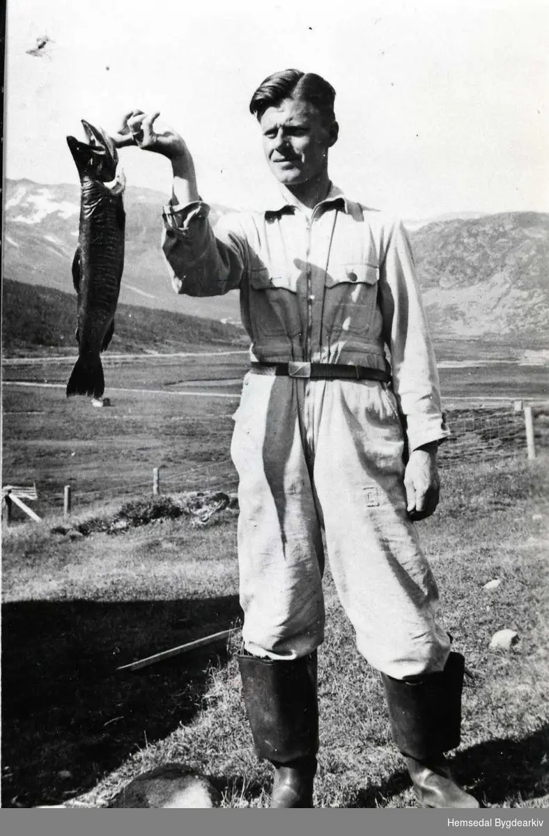 Biletet er teke kring 1940.
Dette er ein bymann som ferierte på Flatahytta i Hemsedal. Fisken er teken i Storeskarvatnet.