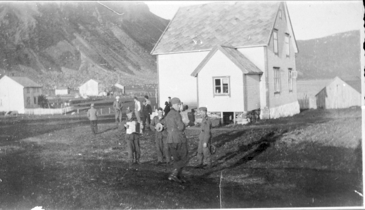 Tyske soldater og norske sivile fotografert ved bygninger på Indre Elgsnes. Fjell i bakgrunnen.
