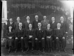 Gruppe kvinne og menn oppstilt utenfor hus. Skiptvet 1936.