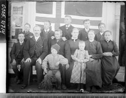 Gruppebilde av fem menn, tre kvinner og fem barn foran et fl