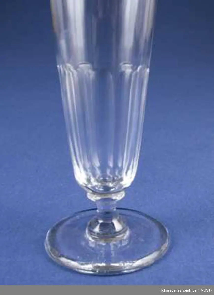Sett med 7 champagneglass med vannrette riller nederst på klokken. Innsvinging på stetten og med liten for.
Glasset er muligens gammelt. På slutten av det 1800-tallet produserte Hadeland glass med samme form og omtrent samme høyde og kalte det for "seltersglass".