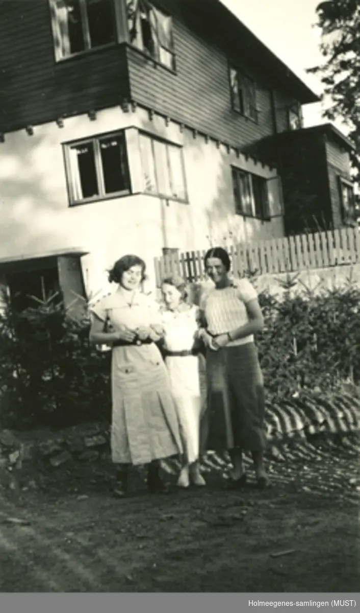 Tre unge kvinner foran et bolighus i funksjonalistisk stil.
