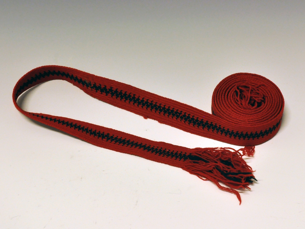 Drakten består av stakk, forkle, 2 trøyer, 2 brikkevevde belter.
C) Brikkevevet band - hårband. Rødt og sort. Fra protokoll.