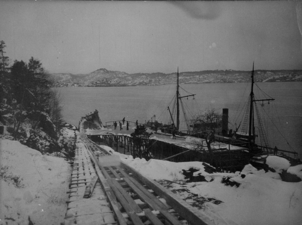 Isblokkene på ned til lastplannen. Bukken som stopper blokkene sees tydelig i enden av renna. Dampskip ligger til kai. Bjelkevik januar 1911.