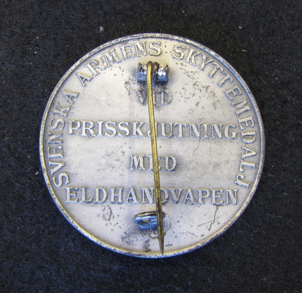 Svenska armens skyttemedalj tilldelad Karl-Fredrik Nyström "vid prisskjutning med eldhandvapen".

På medaljens åtsida, två korslagda gevär- Ovanför dessa en krona. Bakom gevären en lagerkrans som är träd genom två kronor. En tredje ligger ovanför där lagerkransen knyts samman av ett band.

Medaljen ingår i en samling märken och medaljer sittande på en tavla med märken, framförallt skyttemärken.

Karl-Fredrik Nyström var aktiv fritidsskytt och var en av de drivande för att starta Vänersborgs skytteklubb.