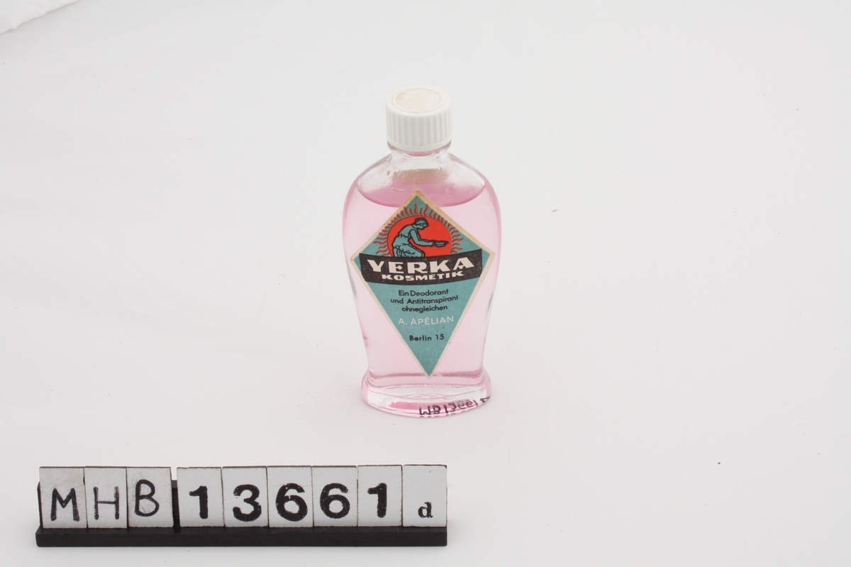 Deodorantflaske med ovalt tverrsnitt. Flasken vokser i omkrets oppover, og smalner igjen før halsen. Øverst er en hvit plastkork med riller. På fremsiden er et klistermerke fra produsenten, og bak er et klistermerke fra utsalgssted. Innholdet i flasken har en rosa farge.