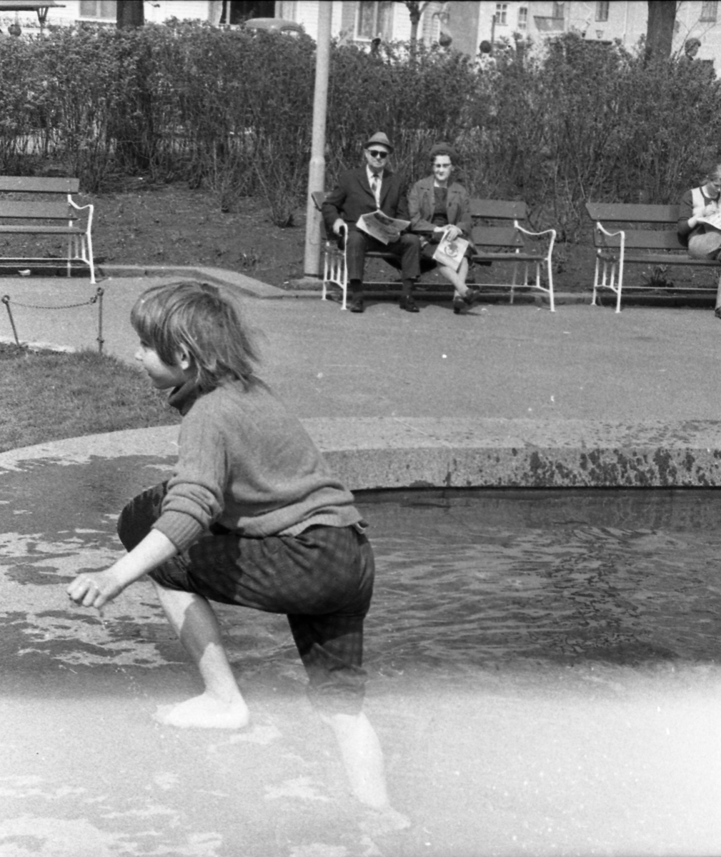 Bilder fra Rådhusparken. Barn som leker i vannet. Flere personer nyter været på benkene i parken.