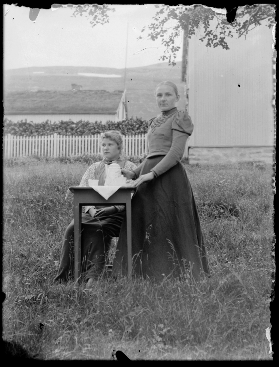 To kvinner ved kaffebord utenfor sorenskrivergården i Tana Langnes, Heimli, gnr/bnr Matr.no.19; L.nr. 4). Vilhelmine Methi (1878-1956) til høyre. Bildet er tatt rundt 1900 av fotograf Johannes Øwre.
