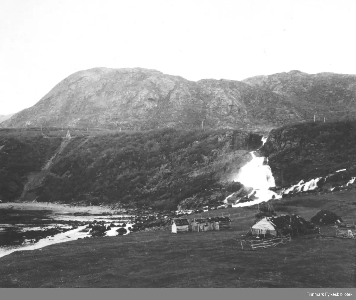 Et bilde fra Adamsfossen i Laksefjorden. Foran står det en torvgamme samt noen mindre bebyggelser. Bildet er tatt på sommerhalvåret.