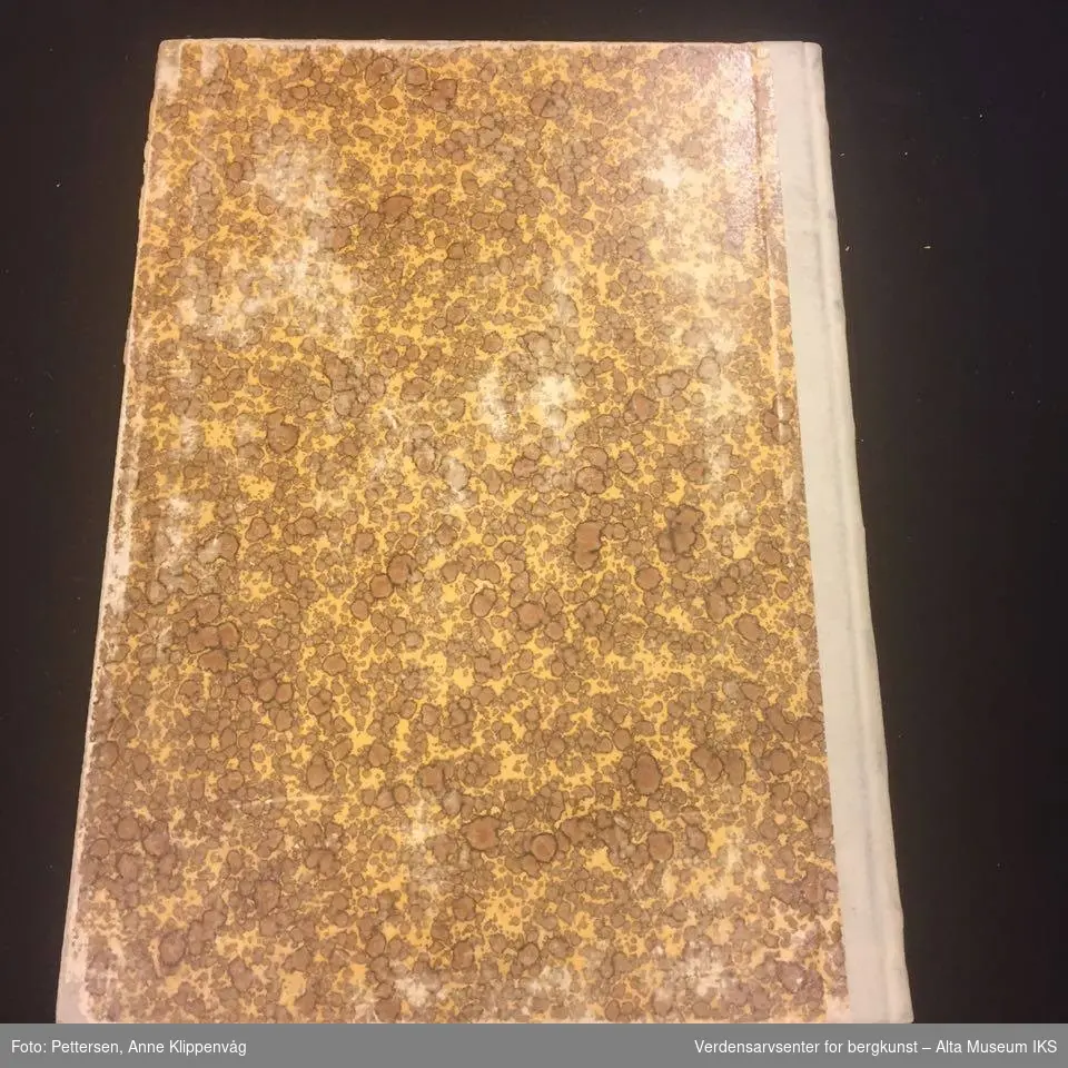 Rektangulær notatbok, innbundet med harde permer. Brunmønstret på forsiden og baksiden.