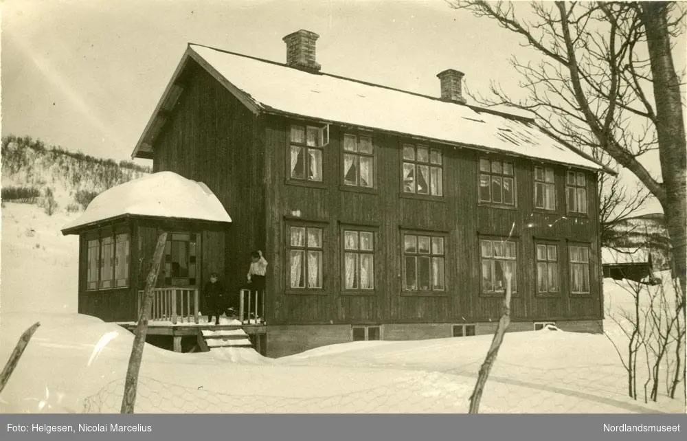 Påsketur til Vatnvatnet 1915. Hus i to etasjer, store krysspostvinduer. To personer sitter på trappa. Snø.