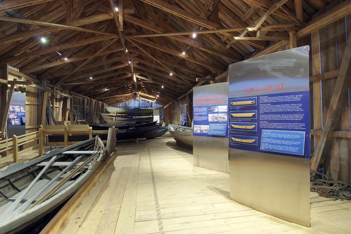 Foto av gamle båter og informasjonsplansjer i gammel bygning.