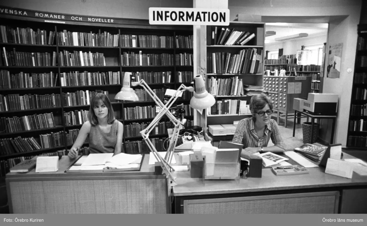 Biblioteket trångbott 29 juni 1972

Vid informationen sitter det två kvinnor vid skrivbord. Bakom dem ser man hyllor med böcker.