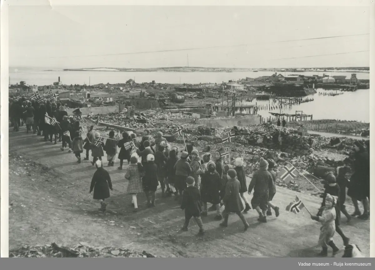 17-mai tog gjennom Vadsøs gater, rett etter krigens slutt. I bakgrunnen ses det ødelagte sentrumsområdet.