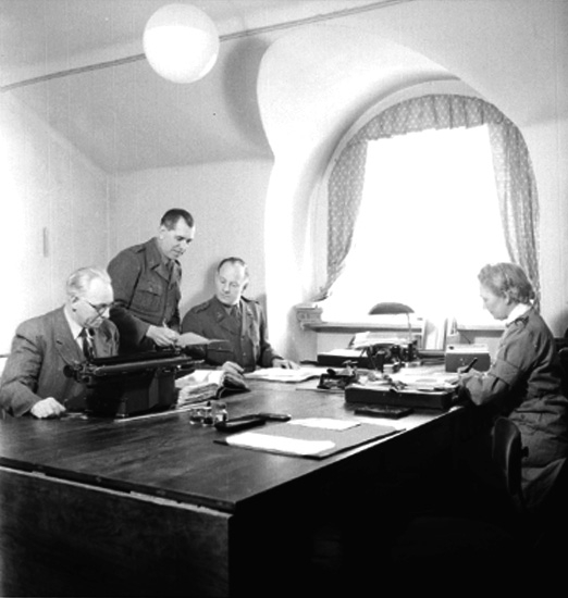 Fo-staben, kontorsinteriör, fyra personer. 
Domänavdelningen vid Fostaben.
Löjtnant E. Brodding, fru Kerstin Nilsson, uppbördsman Å. Göranson och värnpliktig N. Landsjö.
Bilden är förmodligen tagen den 1 mars 1945.