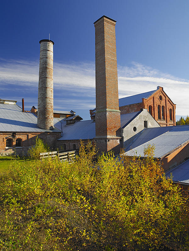 Klevfos Cellulose- & Papirfabrik i sol. De to store mursteinspipene strekker seg mot himmelen.