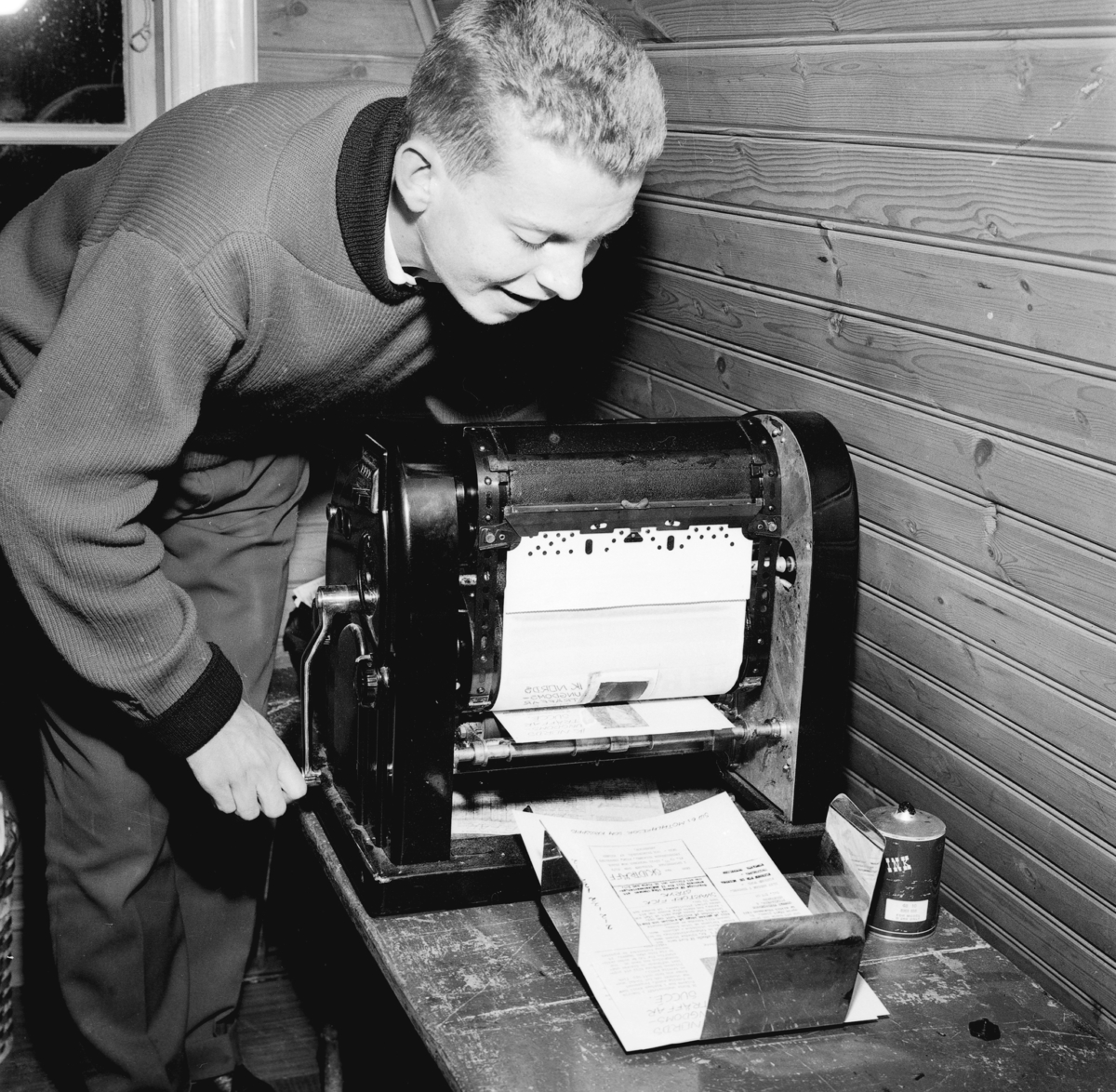 En ung pojke arbetar vid kopieringsapparaten med att trycka tidningen Hakarpsbladet.