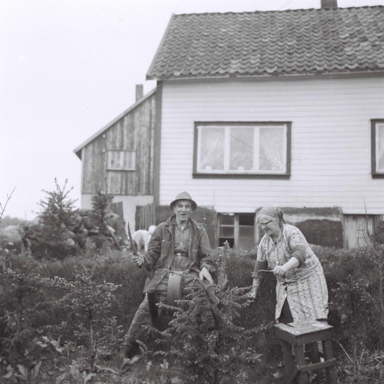 Torbjørg og Ingvald Skårland ved slipesteinen i 1957. Heimehuset på Langholen bak