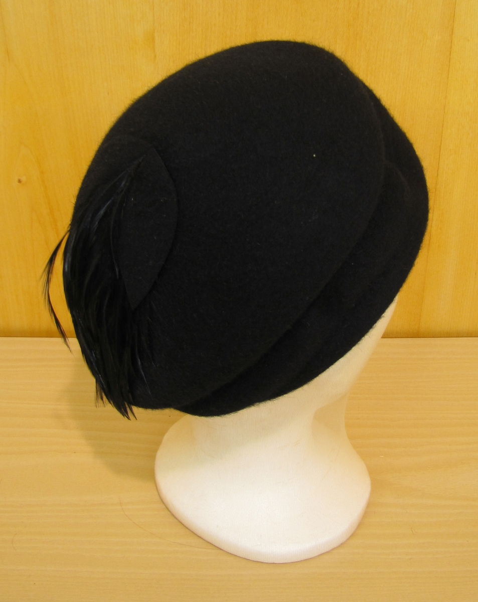 Liten rund hatt utan brätte, monterad med svarta fjädrar.