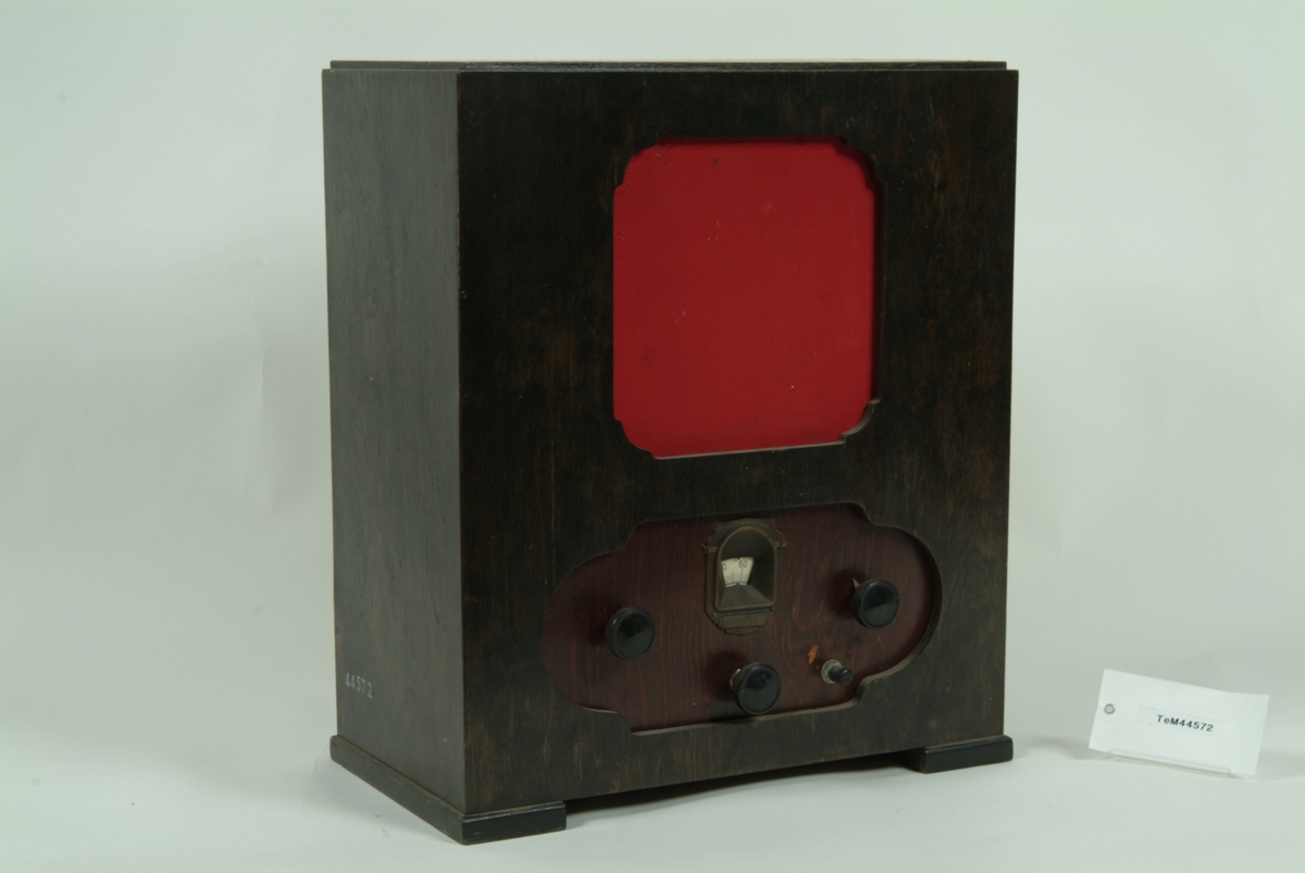 Radiomottagare med inbyggd högtalare för batteridrift, troligen hembyggd. Radiomottagaren är byggd i ett hölje av trä med röd textil framför högtalaren framtill.