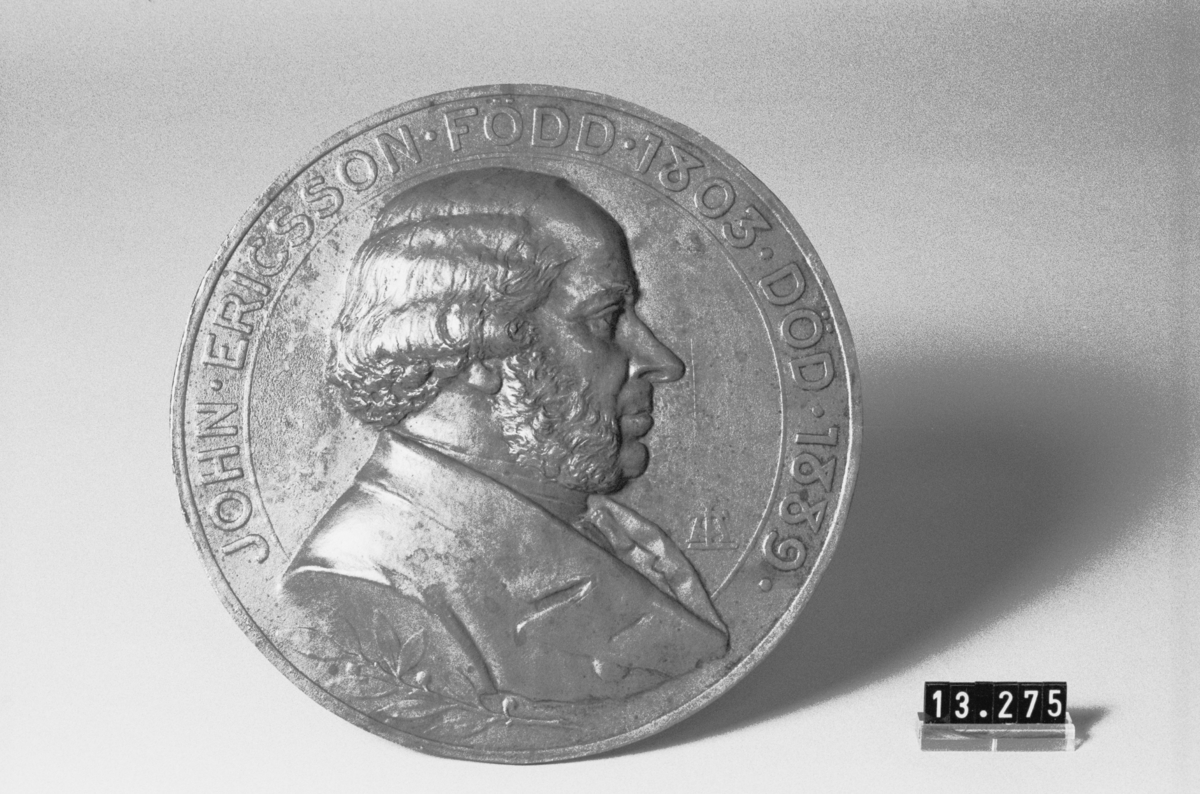 Medaljong, gjuten i brons, över John Ericsson, höger profil, signerad LA. "John Ericsson född 1803 död 1889".